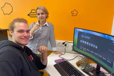 Kaksi henkilöä näytön edessä.